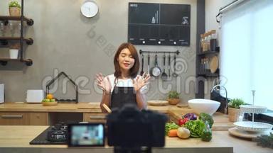 年轻的亚洲女人在厨房里用<strong>相机录制</strong>视频。 微笑的亚洲妇女从事食品博客概念。
